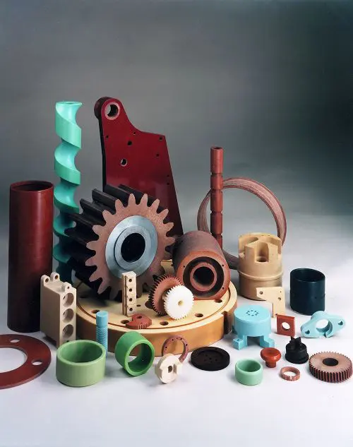 Assorted colorful plastic and tufnol machine parts, gears, and rings arranged on a neutral background.