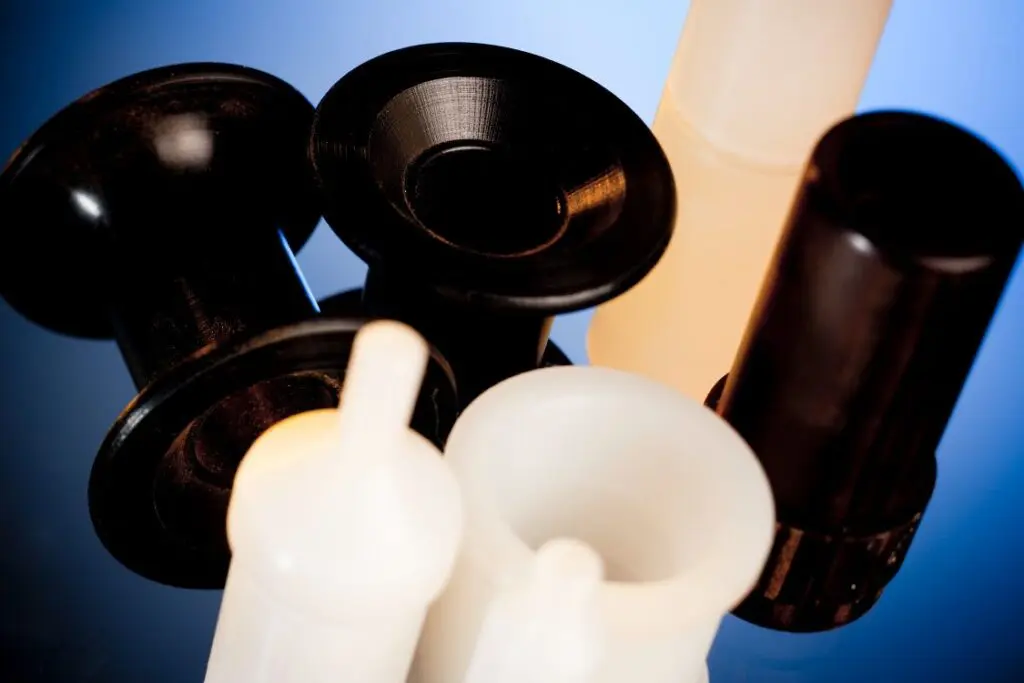 Close-up of black and white thermoplastic materials laboratory containers and adapters on a reflective blue surface.