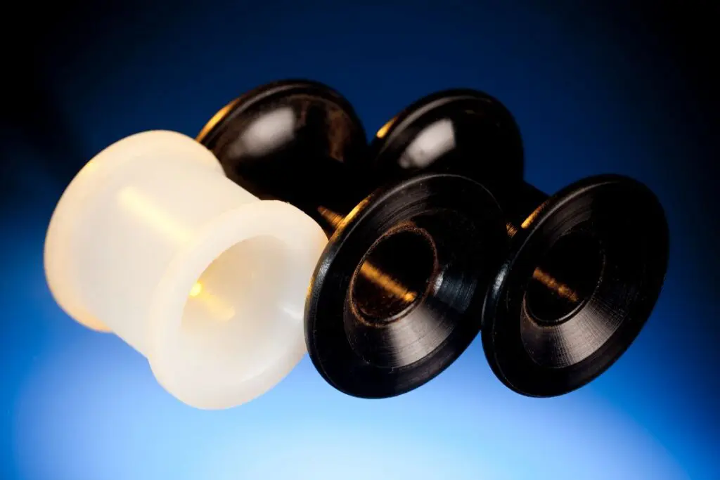 Three plastic spools, made from thermoplastic materials—two black and one white—are arranged on a blue gradient background.