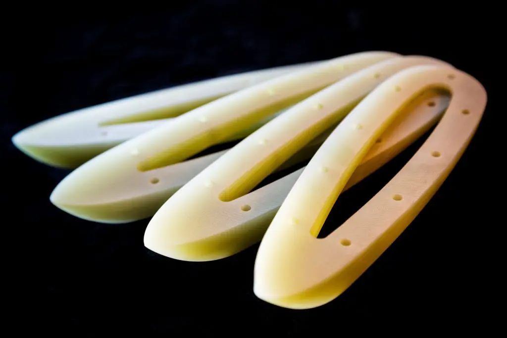 Four elongated, oval-shaped 3D-printed plastic parts crafted from SRBGF material, each with holes, arranged on a dark background.