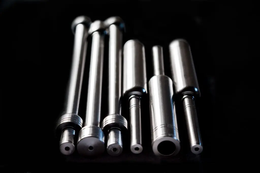 Six shiny metal rods with threaded and hollow ends, often used in conjunction with thermoplastic materials, are arranged on a black background.
