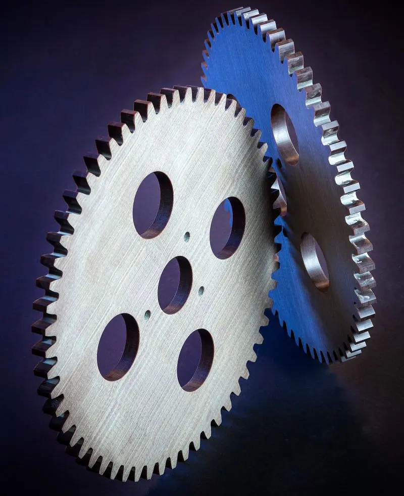 Two large laminated gears with circular cutouts stand upright against a dark background.