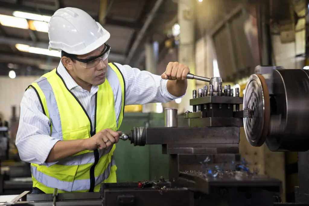 Man in safety gear operates a lathe machine, precisely shaping tufnol components in an industrial workshop setting.