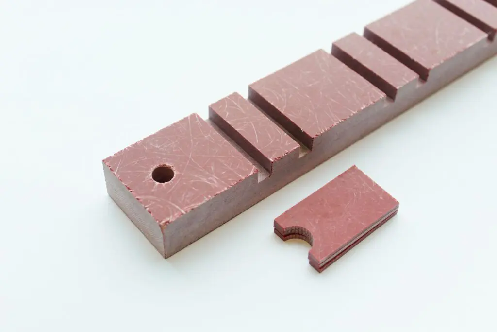 Rectangular reddish-brown blocks with grooves and one hole, made from durable Polyester Glass Mat Laminate Sheets, on a white background.