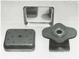 Three metal stamping dies are arranged on a flat surface, with varying shapes and holes visible.