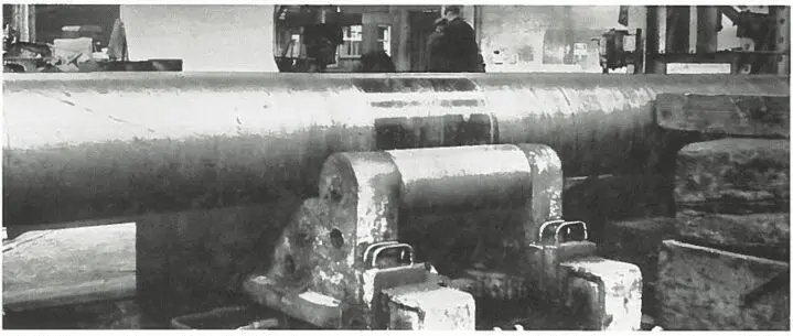 Large metal cylinder supported by heavy machinery in an industrial workshop, with workers in the background.