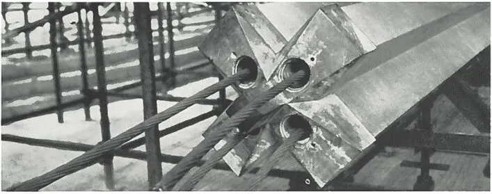 Close-up of steel cables anchored in a concrete structure, part of a bridge or construction site.
