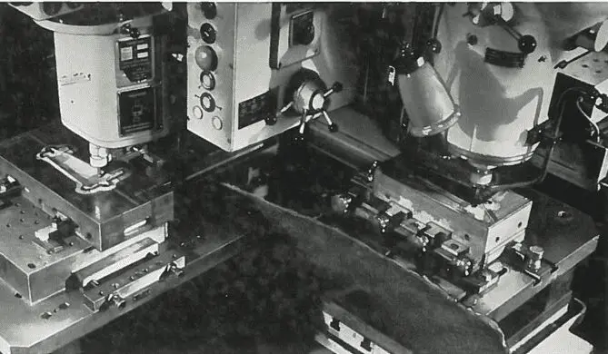 Picture9 Two industrial machines with control panels and clamps, processing metal parts in a manufacturing setting.