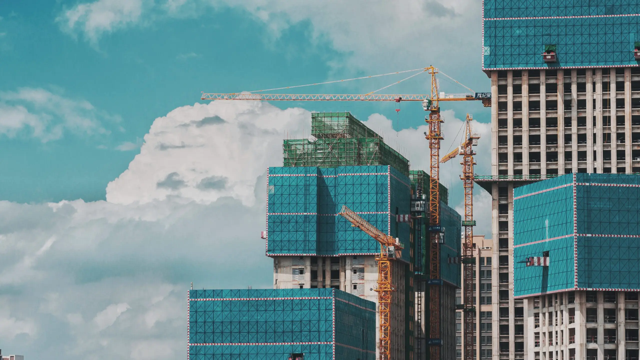 c-dustin-91AQt9p4Mo8-unsplash High-rise buildings under construction with cranes and blue safety netting against a cloudy sky, showcasing the use of laminated plastics for enhanced safety and durability.