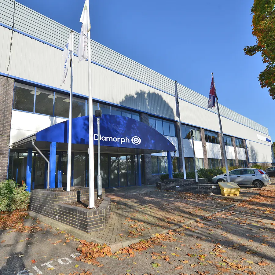 Modern office building with a blue Diamorph sign, three flags, parked cars, autumn leaves on the ground, and a reputation for pioneering non-metallic engineering materials.