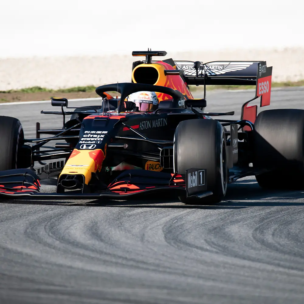 A Red Bull Racing Formula 1 car, utilizing advanced non-metallic engineering materials, drives on a racetrack during daytime.