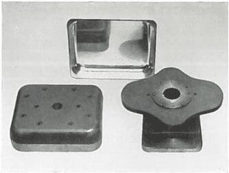 Three metal stamping dies are arranged on a flat surface, with varying shapes and holes visible.