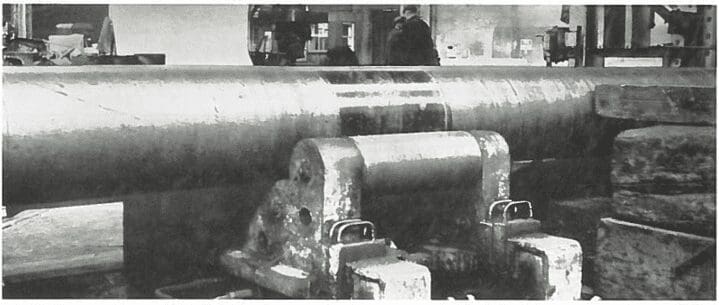 Large metal cylinder supported by heavy machinery in an industrial workshop, with workers in the background.