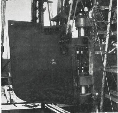 A large metal object labeled “42 tons” is suspended by cables and machinery on an industrial site.