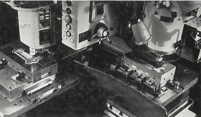 Two industrial machines with control panels and clamps, processing metal parts in a manufacturing setting.