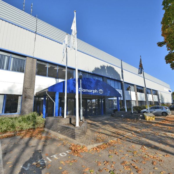 DSC_9676 Front view of a commercial building with a blue Diamorph sign—experts in non-metallic engineering materials—flagpoles, and parked cars on an autumn day.